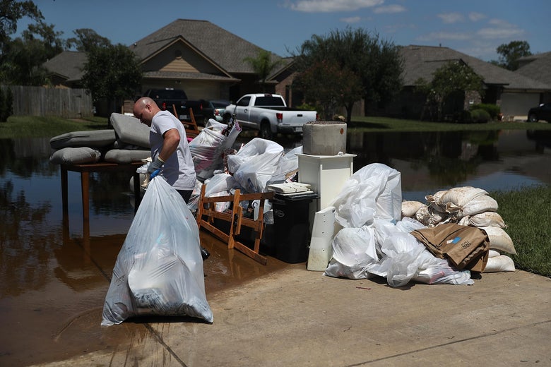 Justin Davison pulls a trash bag full of flood-damaged items to a trash pile as he helps a friend clean out his flooded home.